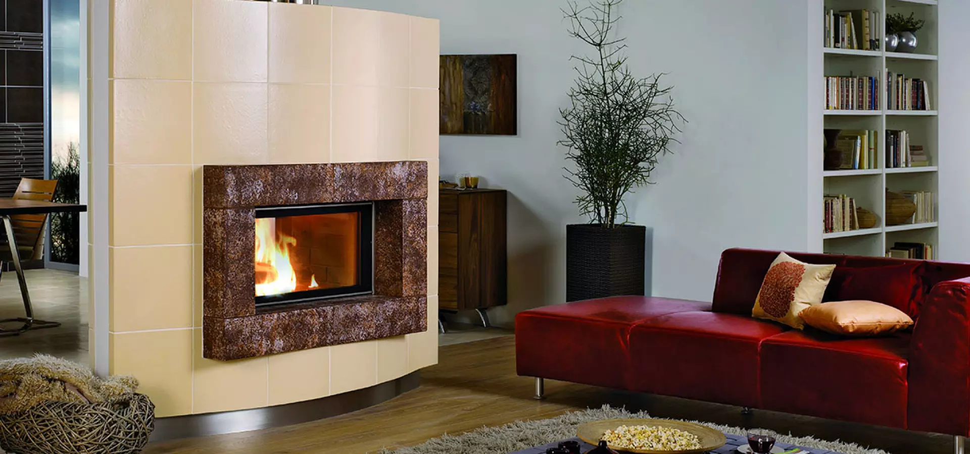 Moderner Heizkamin mit keramischer Verkleidung in hellem Wohnzimmer, rote Design-Couch im Vordergrund.