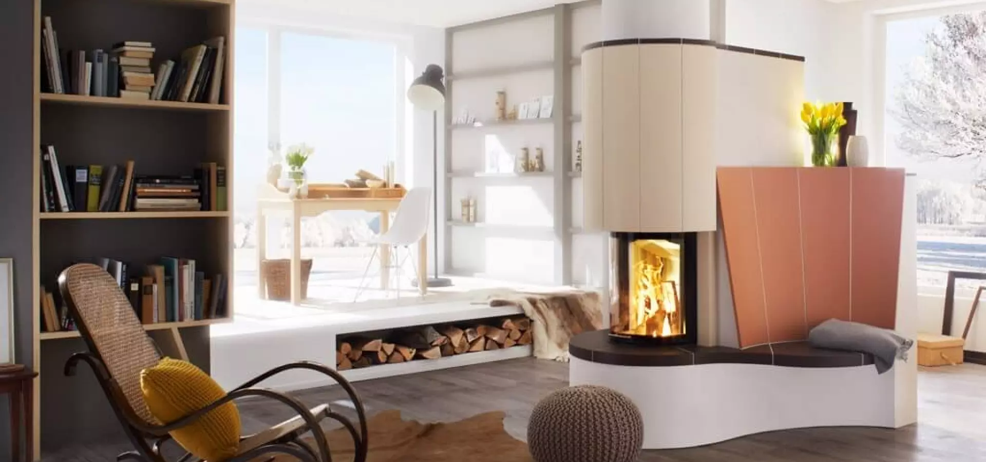 Helles Wohnzimmer mit maßgefertigtem Kachel-/Speicherofen: ein zweiseitig verglaster Eckkamin mit abgerundeter, cremefarbener Verkleidung und geschwungener Ofenbank; viel Tageslicht, Bücherregal und Holzlager