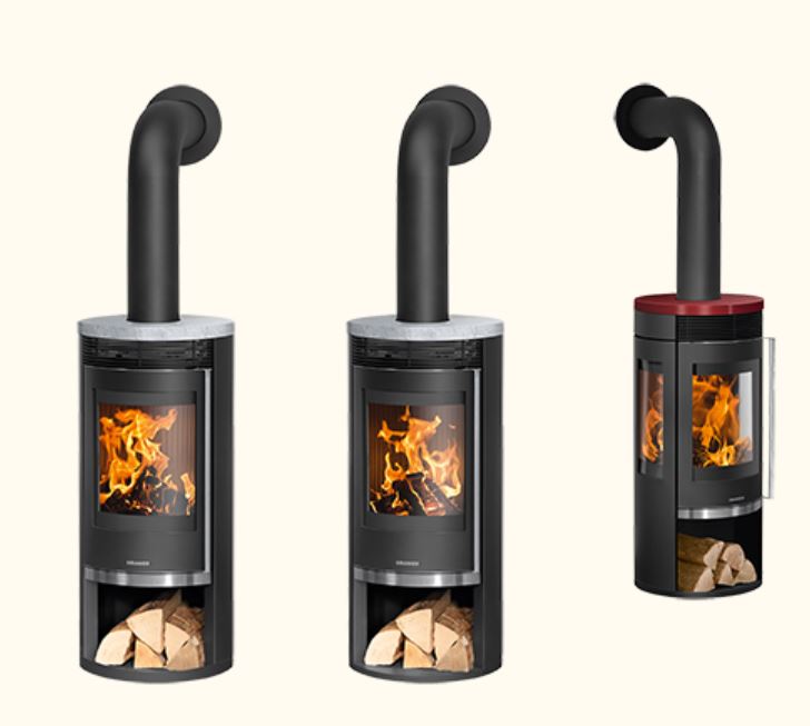 Freistehender, schlanker Rundofen mit heller Natursteinverkleidung. Schwarze, halbrund gebogene Glasfront, darüber eine offene Ablage/Nische – insgesamt eine ruhige, minimalistische Optik.