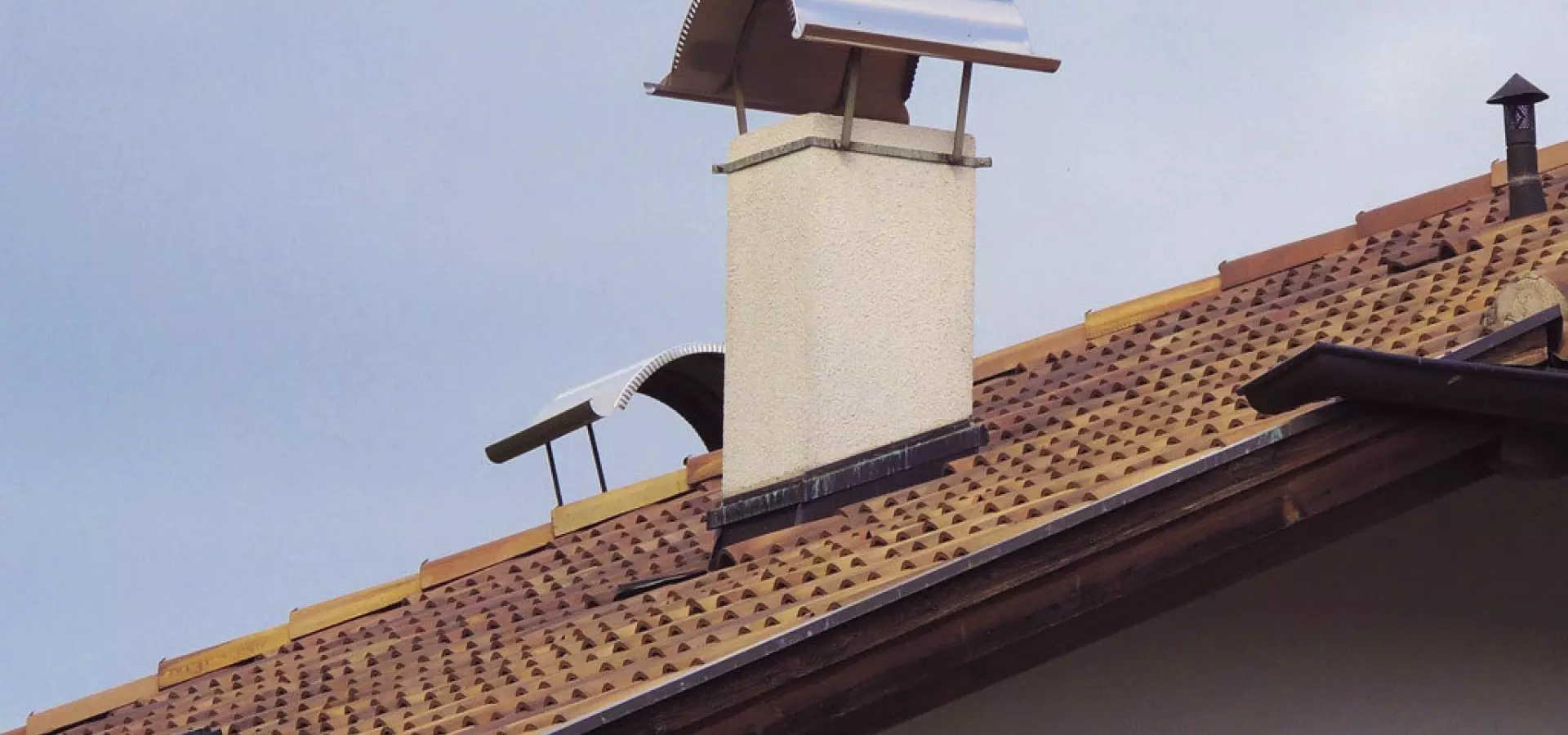 Schornstein mit Edelstahl-Regenhaube auf geneigtem Ziegeldach – Schutz vor Wind und Regen